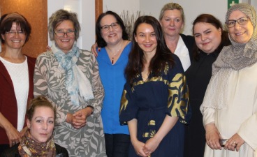 Gruppenfoto des letztjährigen Organisations-Teams des Diversity-Tages. Acht Personen stehen in einem Innenraum. Die Gruppe ist vielfältig gekleidet. Im Hintergrund erkennt man Holztüren und einige Pflanzen, was dem Raum eine warme und einladende Atmosphäre verleiht.